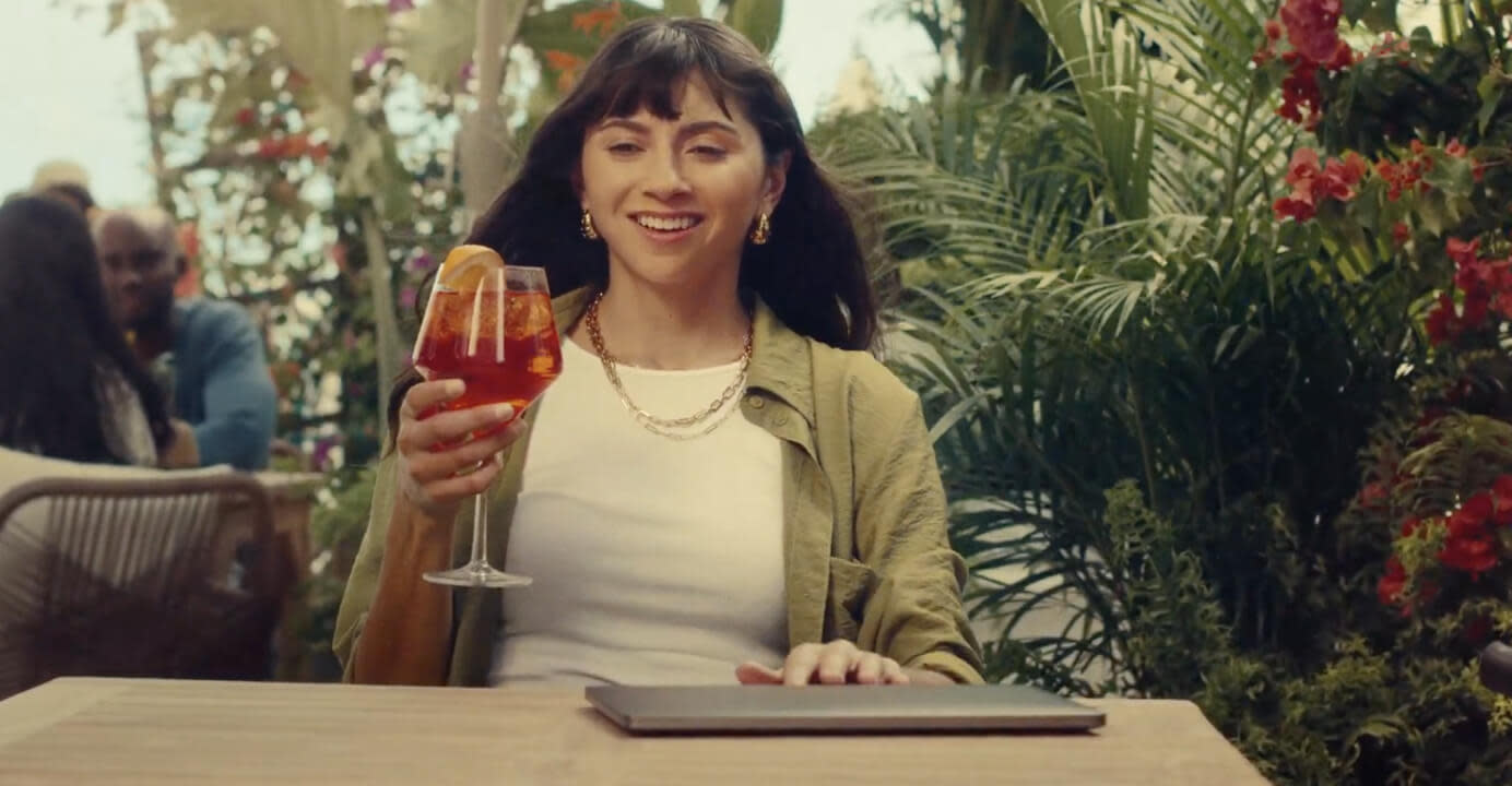 Woman lifts a cocktail with a closed laptop on the table