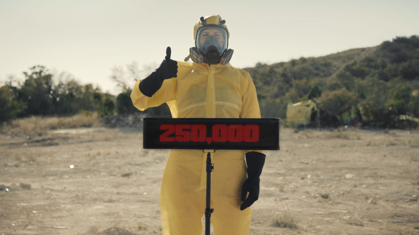 Hazmat scientist giving a thumbs up in front of a sign saying 250,000