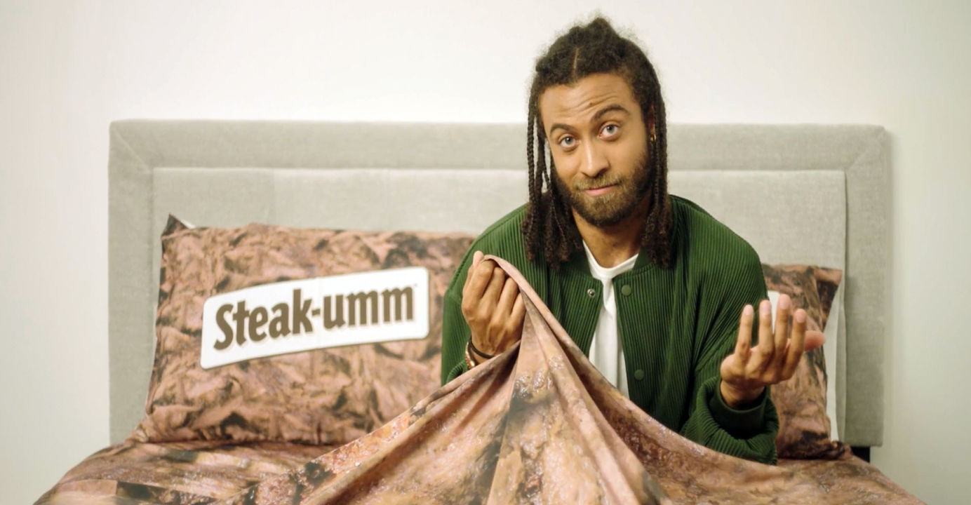 Steak-umm Beef Sheets Campaign video still of a guy sitting in a bed covered with Beef Sheets