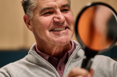 An Aspen Dental patient smiles into a handheld mirror. 
