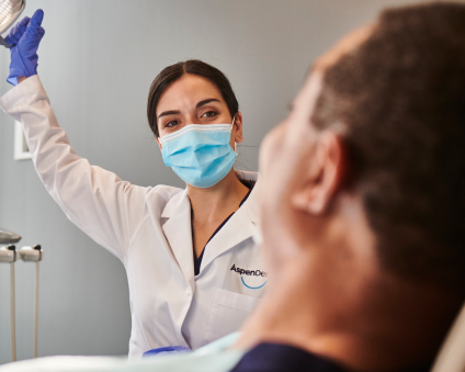 An Aspen Dental doctor looks at a patient in a dental chair. 