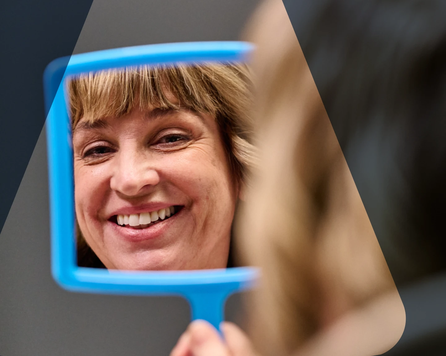 An Aspen Dental veneers patient smiles into a handheld mirror. 