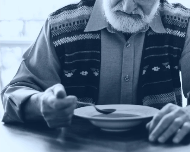 Black and white photo of a senior man sitting and eating with a spoon and bowl of food.