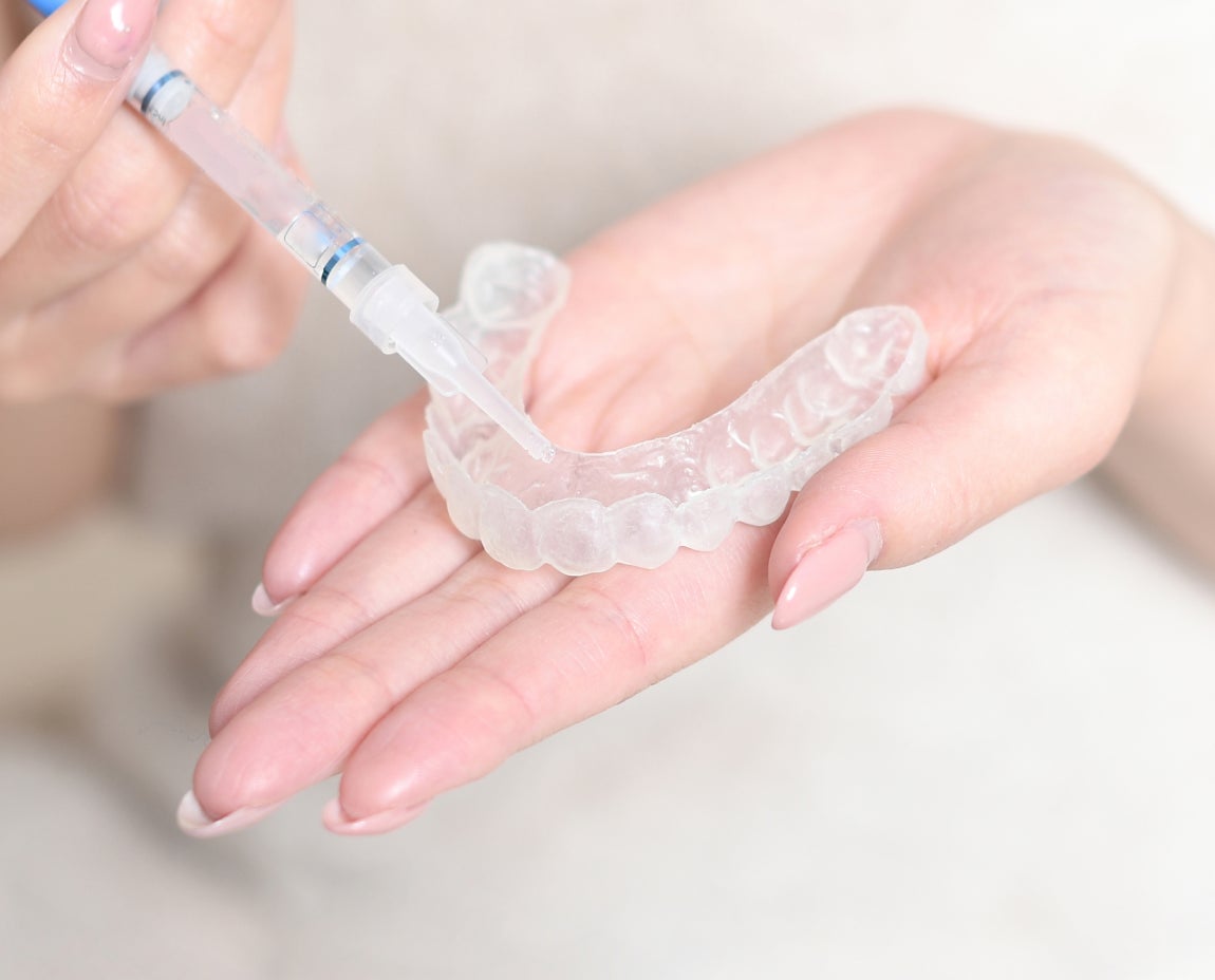 A close-up of a person holding a clear teeth whitening tray and applying whitening gel with a syringe, showcasing the process of at-home teeth whitening treatment.