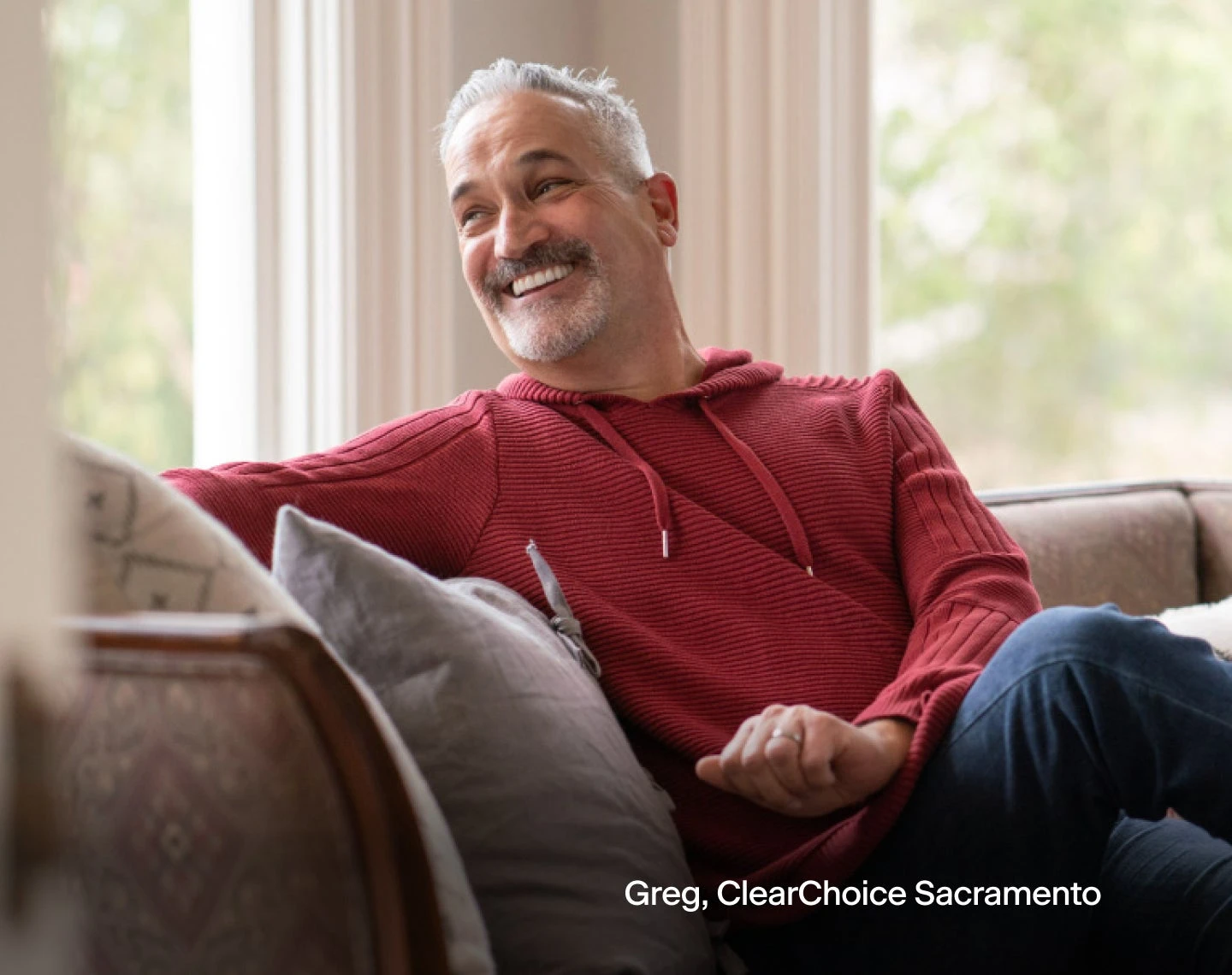 A man in a red hoodie is sitting on a couch.