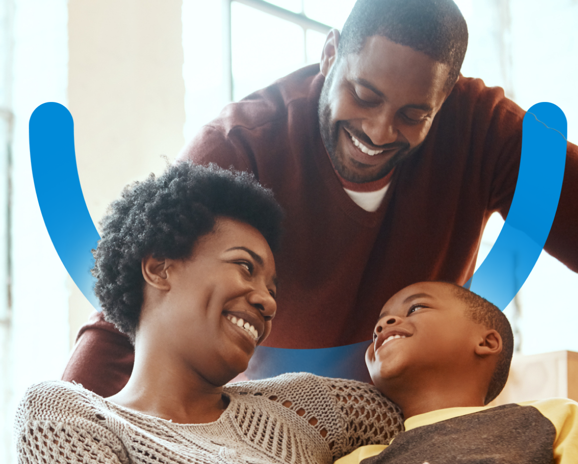 A happy family of three, with a man, woman, and their son, sharing a joyful moment at home, positioned in front of a large window, with an illustration of a blue smile across the image.