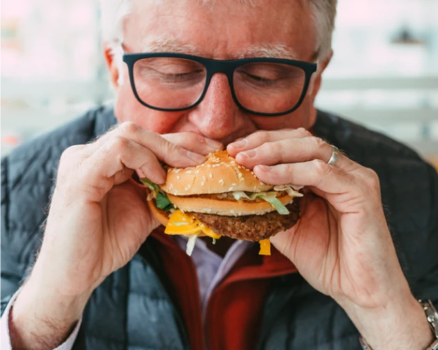  Senior man biting into a cheeseburger.