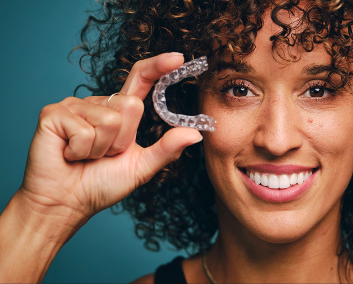 Smiling woman holding Motto Clear Aligners in front of her face, demonstrating how clear aligners work to straighten teeth discreetly.