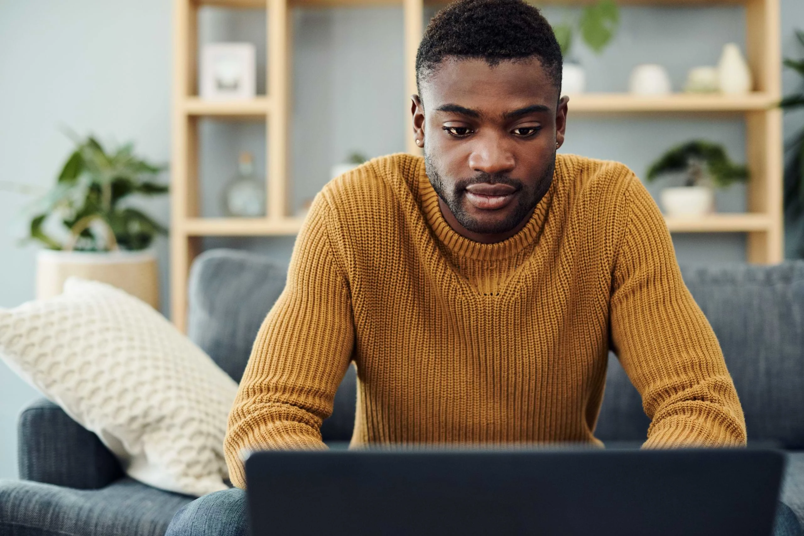 A man sits on a couch using a laptop. 