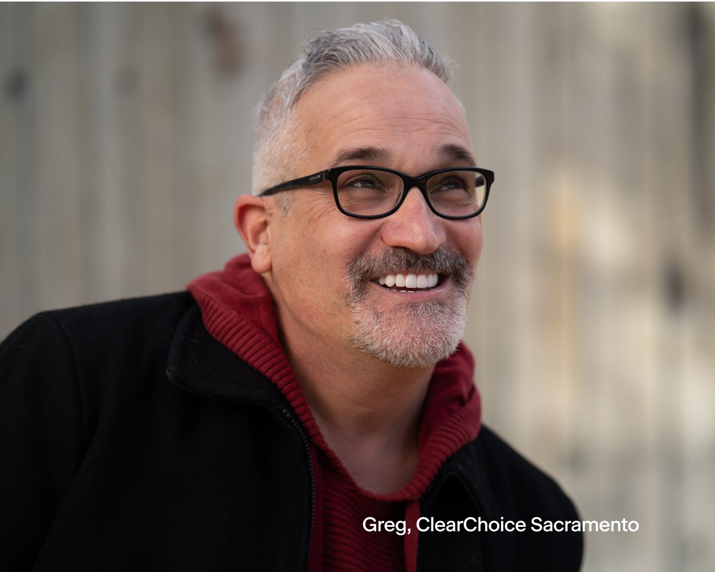 A man wearing glasses and a red hoodie is smiling