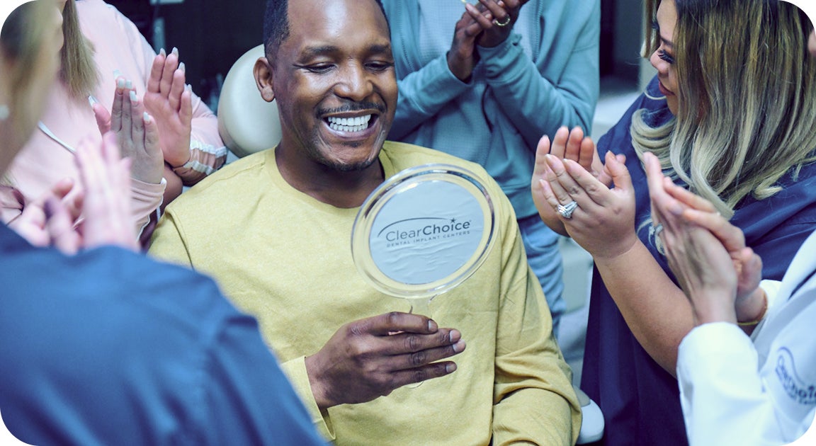 A ClearChoice patient with osteoporosis celebrating his new dental implants post-surgery with friends and family around him.