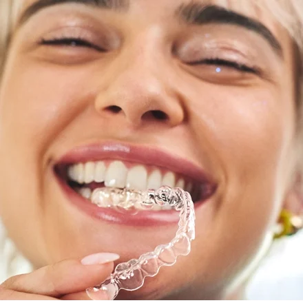 A woman smiles as she playfully bites her Motto Clear Aligners. 