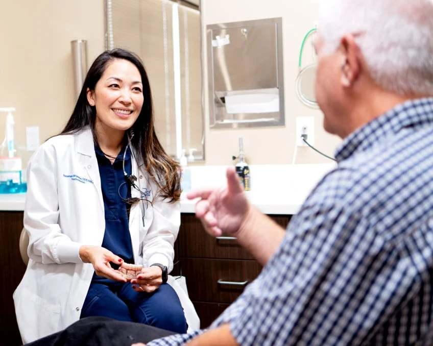 ClearChoice dentist explaining virtual smile design to a patient while holding an upper arch dental implant.