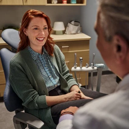 A woman sits in a dental chair talking to a doctor