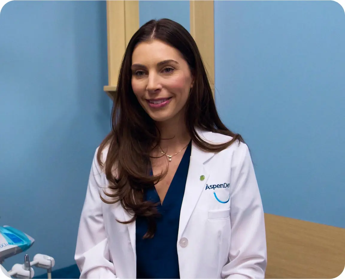 A female dentist in a white coat smiles at the camera, representing professional care for oral health issues like canker sores.