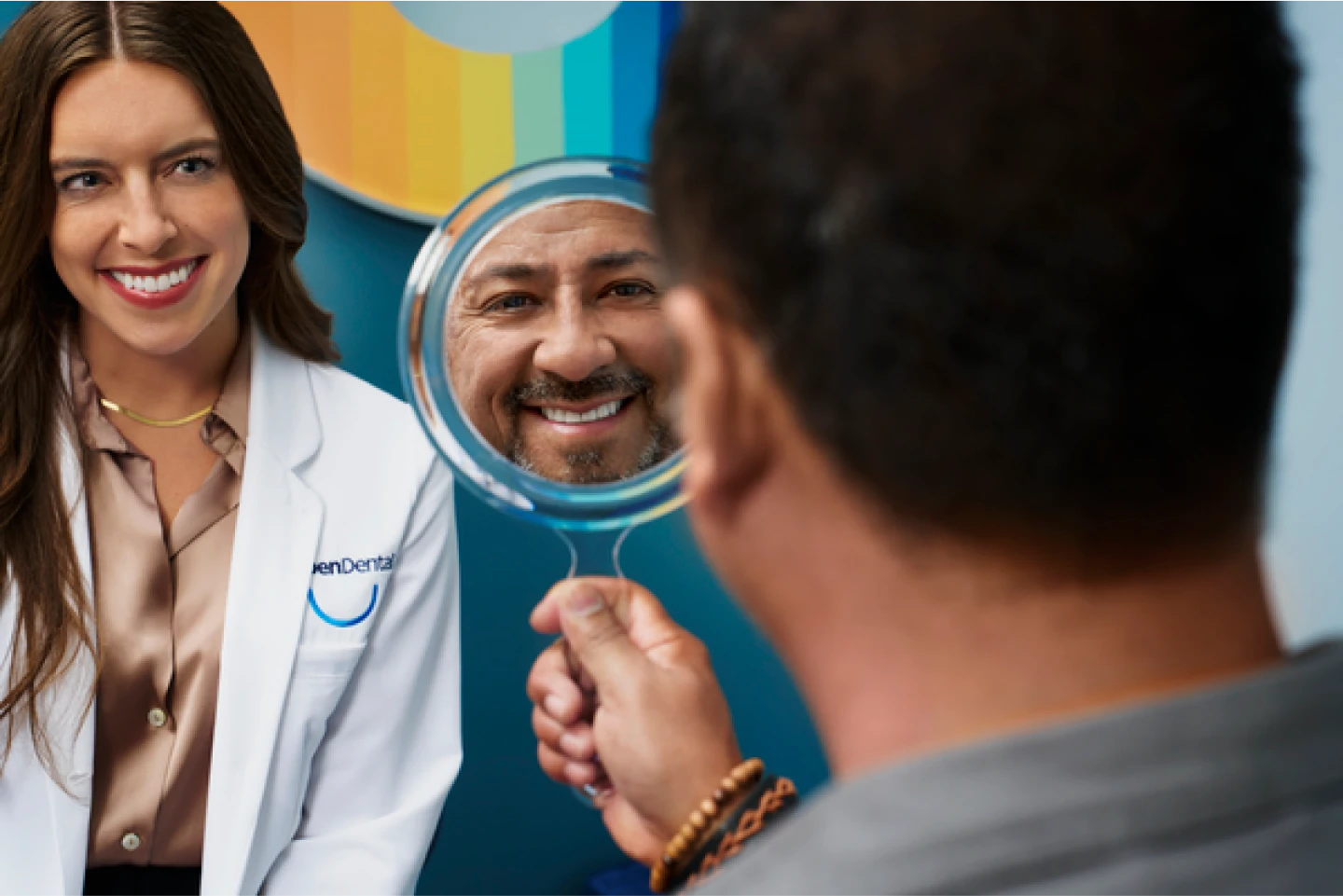 An Aspen Dental doctor smiles as a patient looks at their smile in a mirror. 