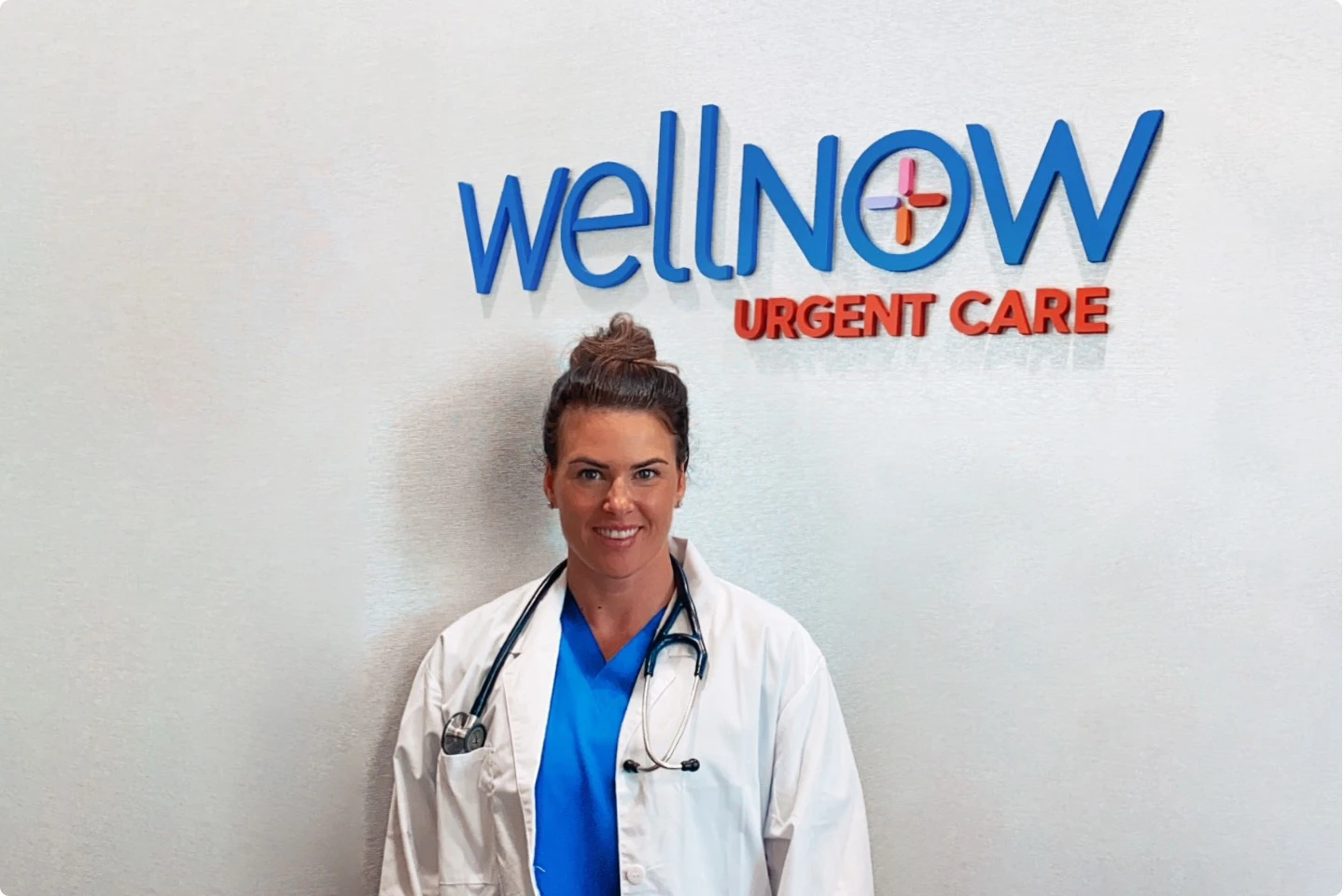 A WellNow Doctor stands in front of a WellNow clinic sign