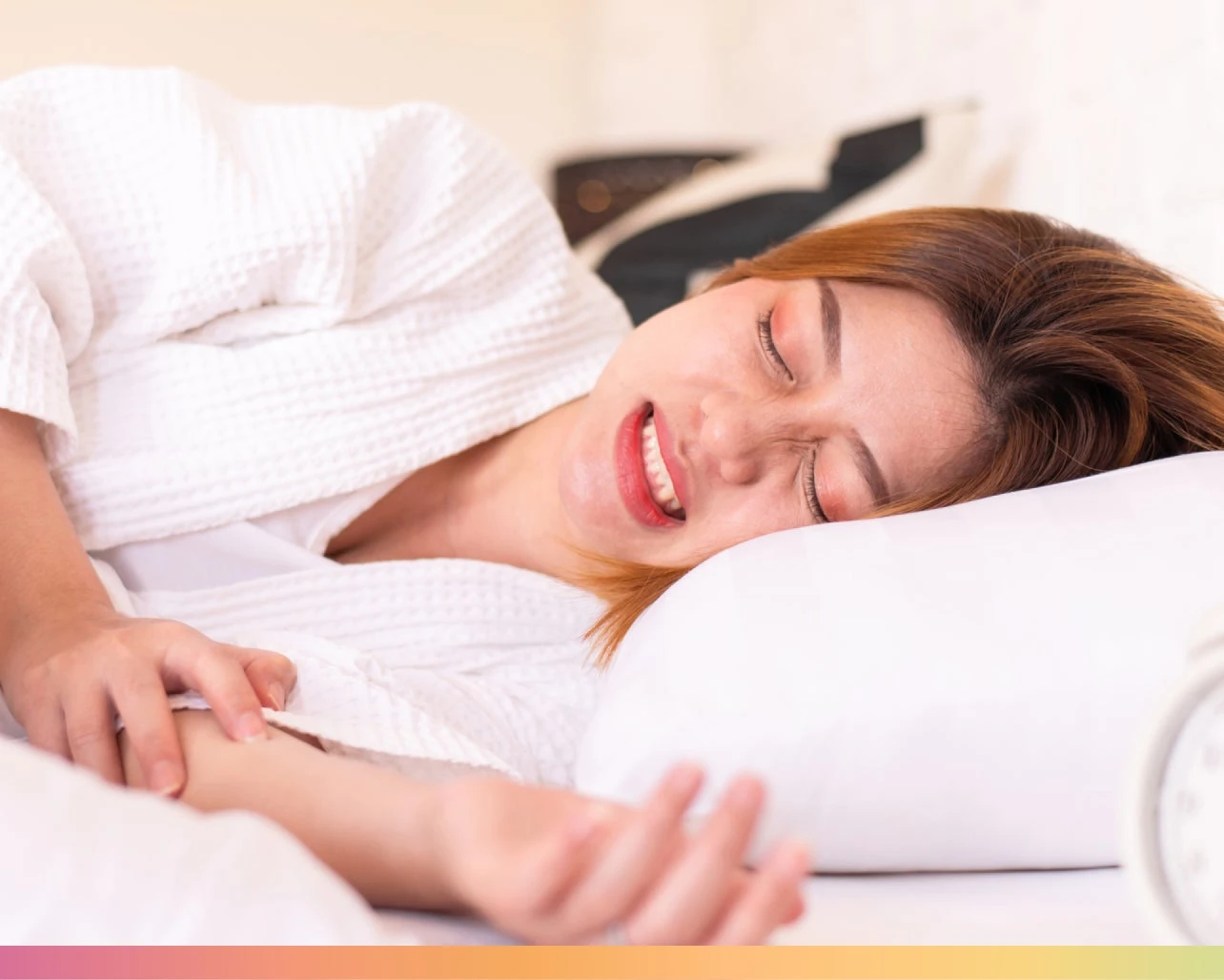 A person in a white robe lies on a bed, appearing to experience discomfort or pain, perhaps from grinding teeth in sleep.