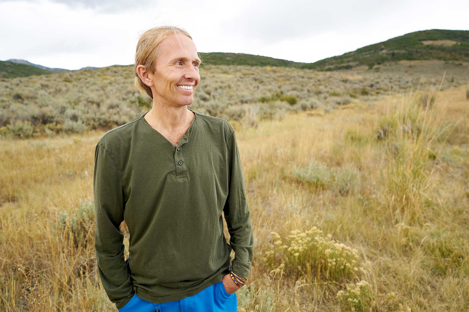 A man in a green shirt is standing in a field with his hands in his pockets