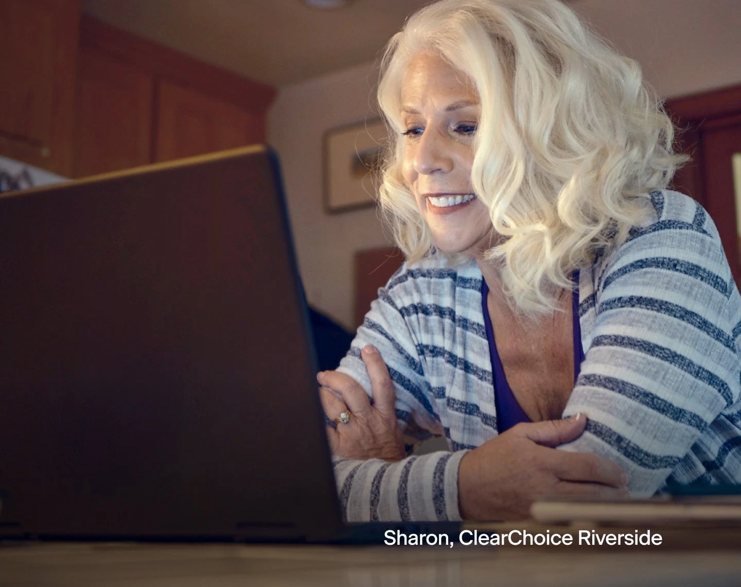 A woman is smiling while looking at a laptop computer with text in the bottom right corner "Sharon, ClearChoice Riverside".