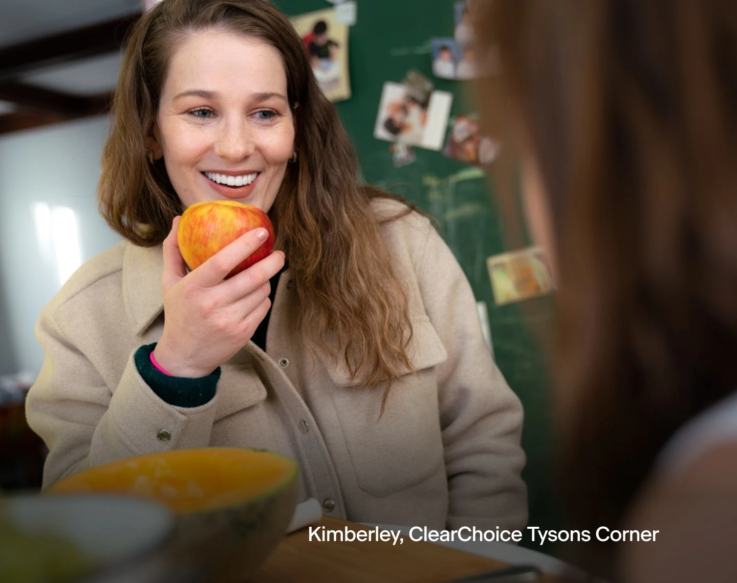 A woman is smiling while holding an apple in her hand