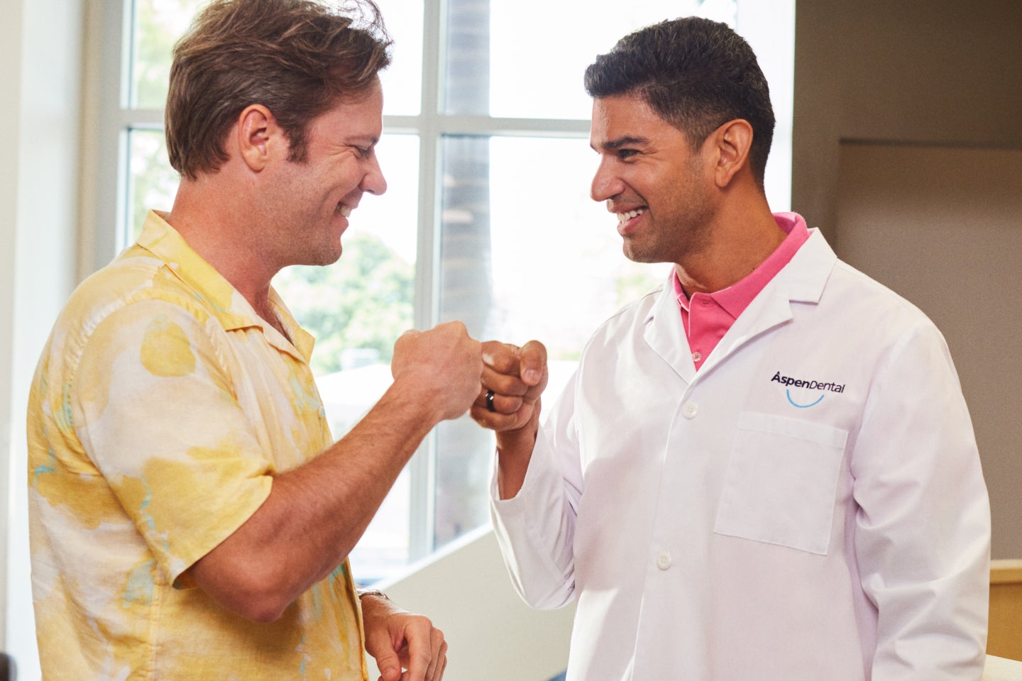 An Aspen Dental dentist fist bumps with a smiling male patient