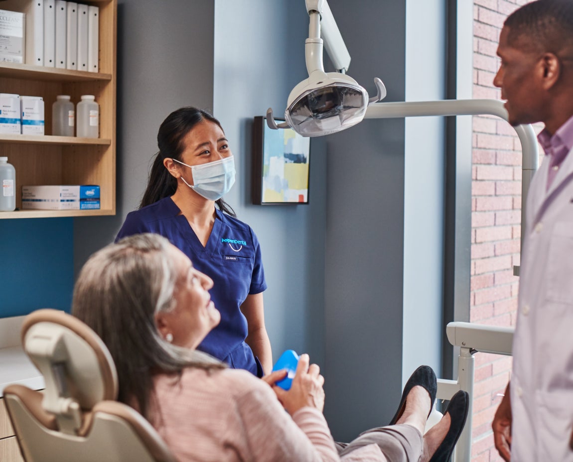 A dental team at Aspen Dental consulting with a patient in a treatment room, explaining proper care and maintenance to extend the lifespan of dental implants.