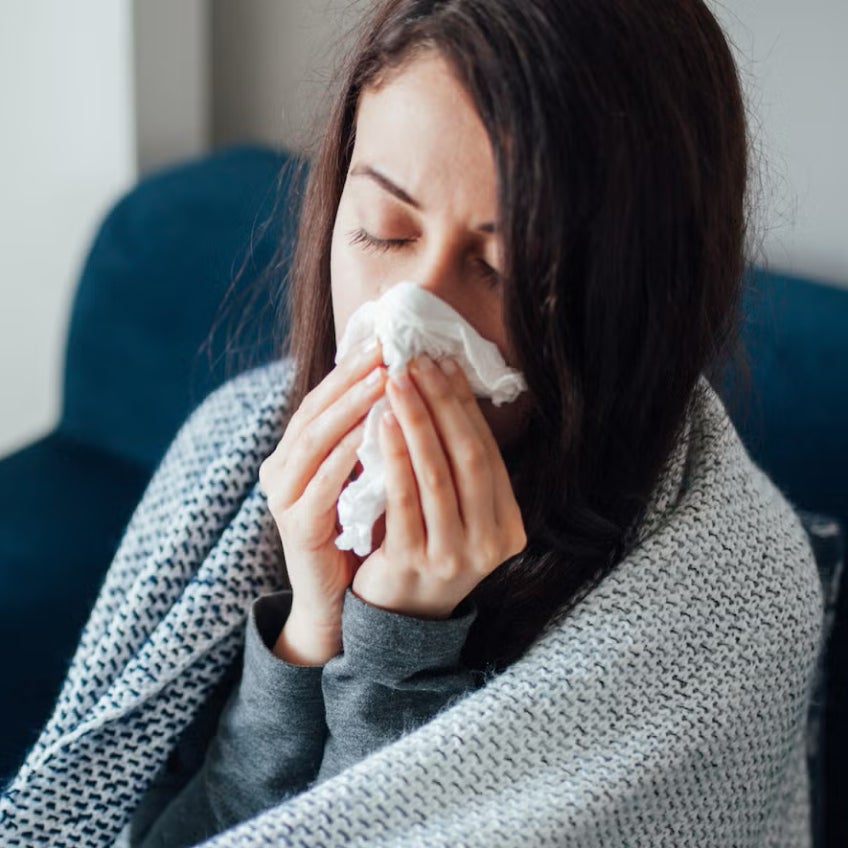 A person with the flu blows their nose into a tissue. 