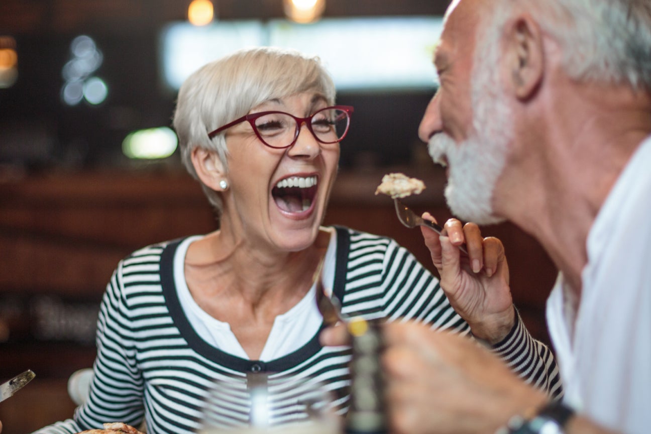  Joyful senior couple laughing together while dining out, highlighting the confidence and quality of life restored with Aspen Dental care.