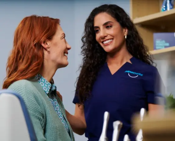 A smiling dental professional in a navy blue uniform warmly engaging with a female patient in a dental office, creating a welcoming and reassuring atmosphere for quality dental care.

