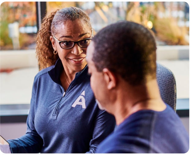 A woman wearing glasses and a sweatshirt with an 'A' logo converses with a man in a dental office.