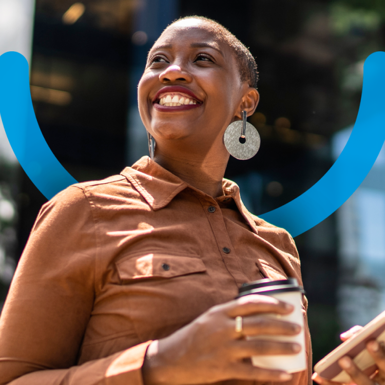 An Aspen Dental dentures patient smiles as she carries a phone and a coffee cup. 