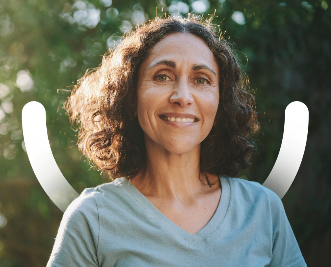 A woman with curly hair and a light blue shirt smiles at the camera, with greenery and sunlight in the background. A smile icon is behind the woman.