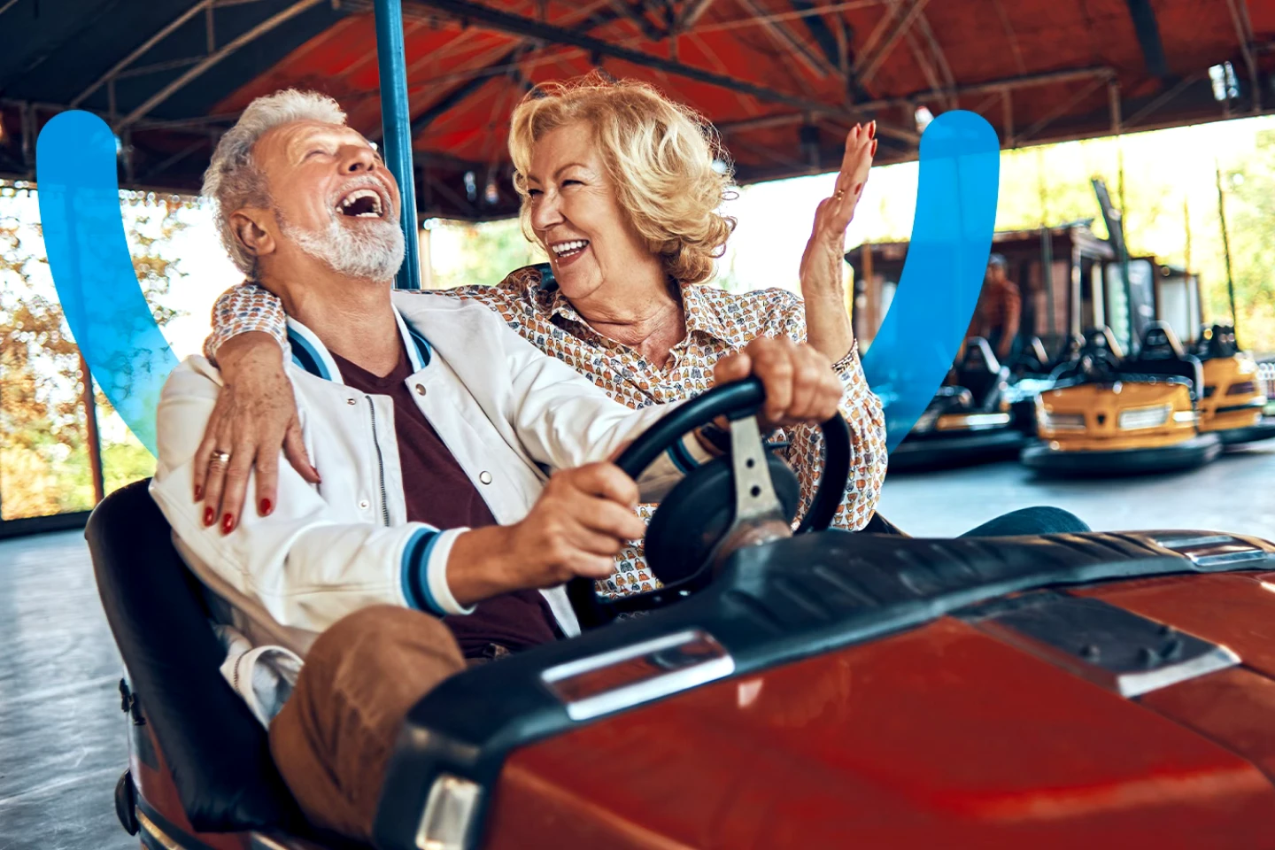 An older couple riding a bumper car at an amusement park with the Aspen dental smile icon on the background.