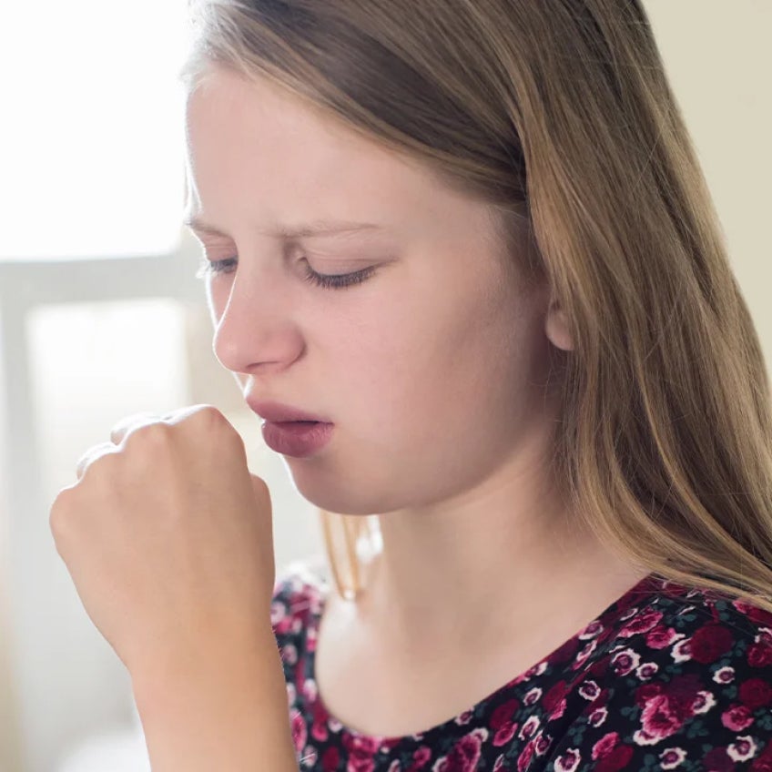A young woman is coughing into her hand
