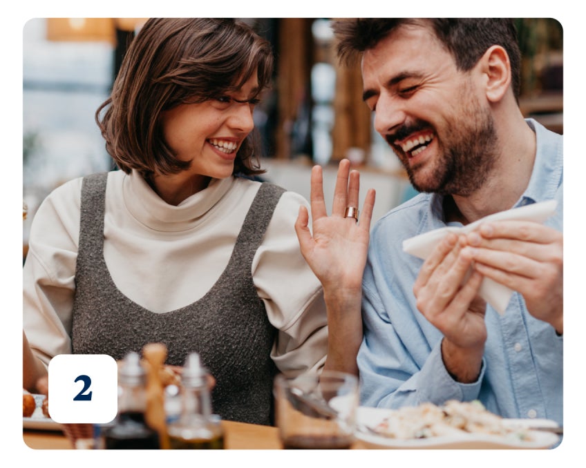 A couple sitting at a table, sharing a joyful moment and laughing, with food and condiments in front of them. A number "2" is displayed in the bottom left corner.