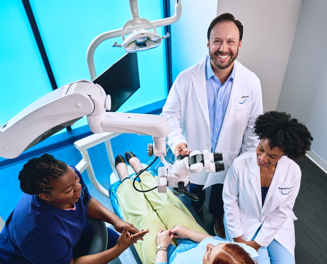 Aspen Dental team consulting with a patient in a dental chair, featuring advanced dental equipment and friendly staff interaction.