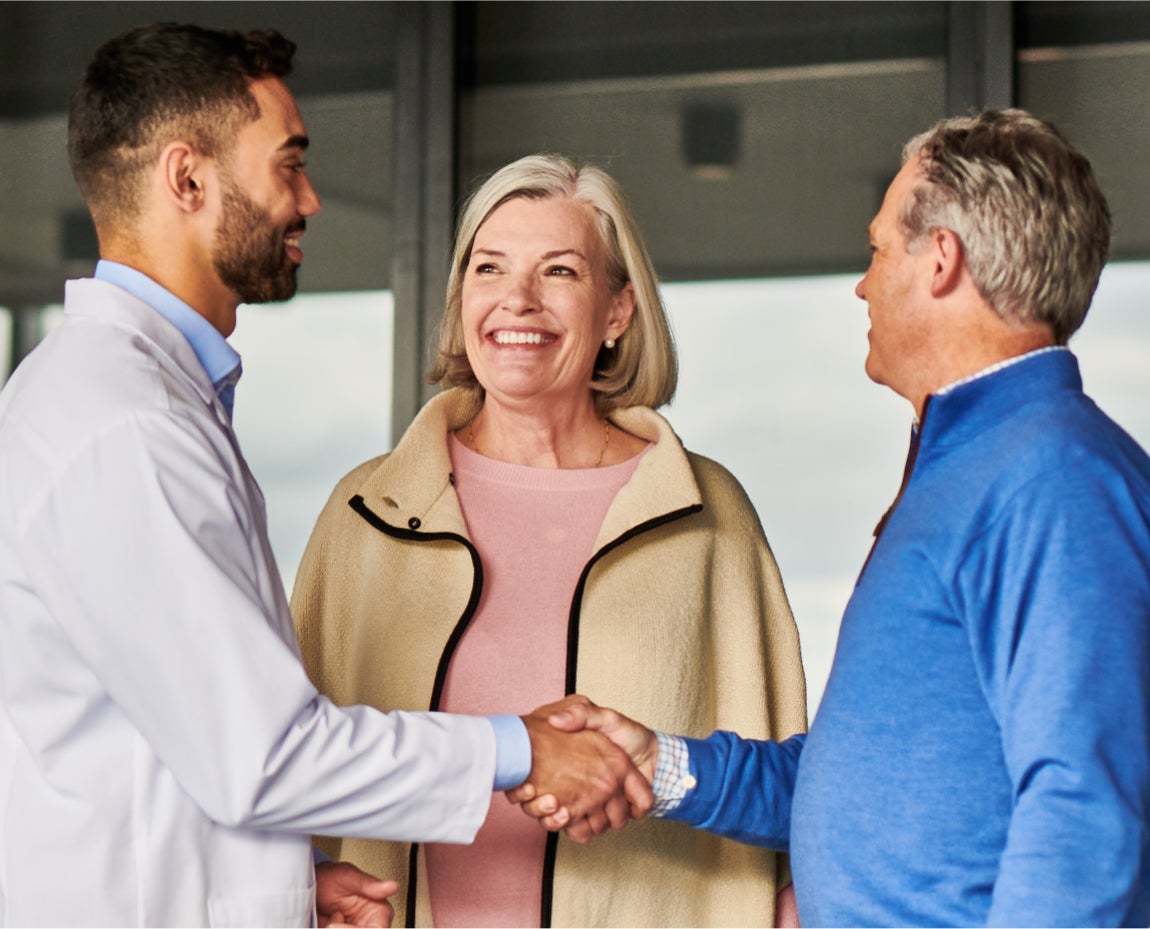 A dentist warmly greeting two patients with a handshake, reflecting friendly and professional care at Aspen Dental.