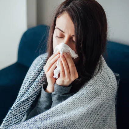 A person with the flu blows their nose and sits on the couch. 