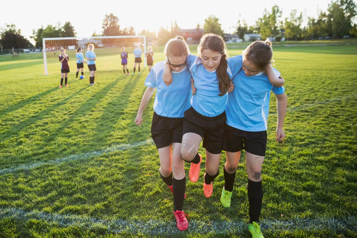 Teammates help an injured soccer player off the field. 