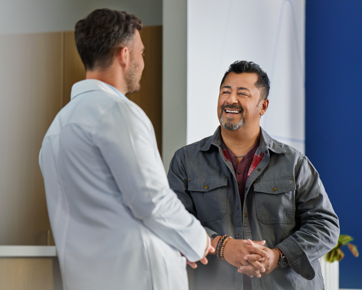 A man in a gray jacket smiling and talking to a dentist in a white coat inside the Aspen Dental office.