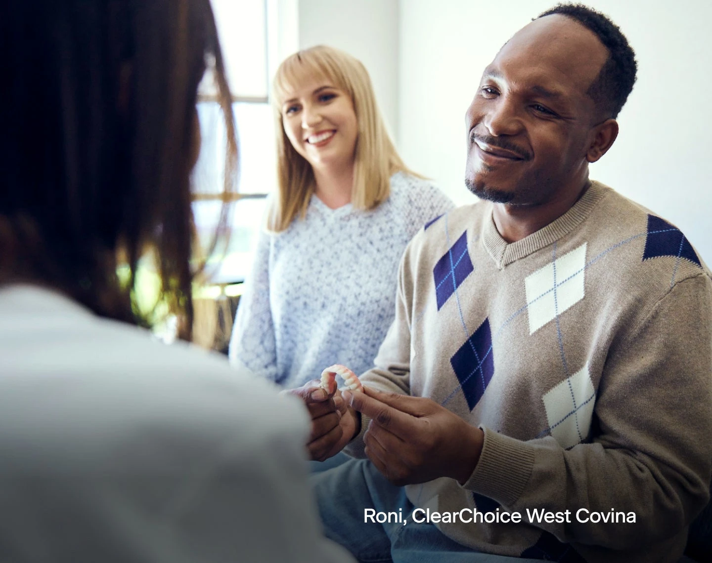 A man in a plaid sweater with a set of dentures in his hand is talking to a woman