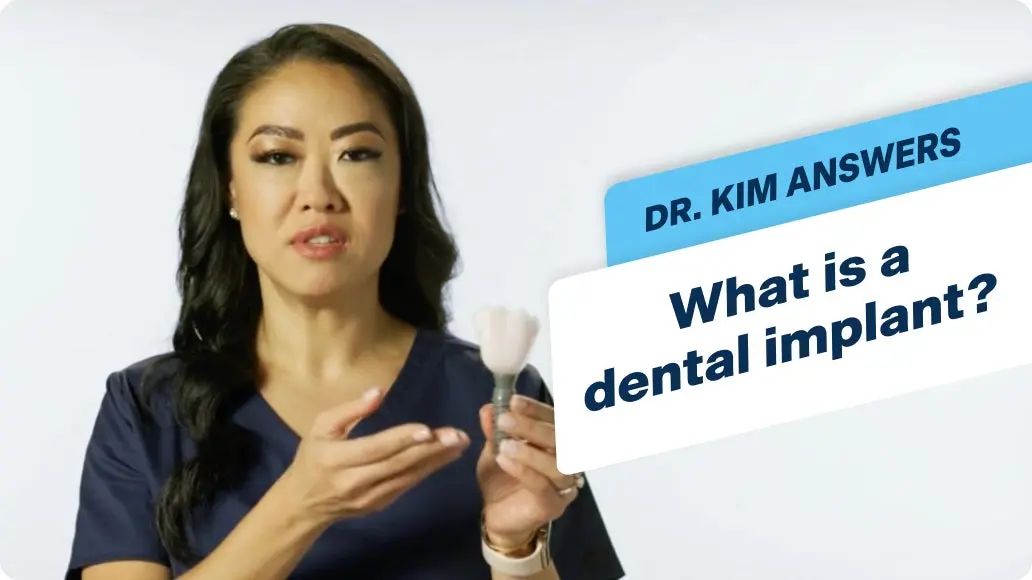 A ClearChoice specialists named Dr. Kim is holding a dental implant in front of a sign that says what is a dental implant.
