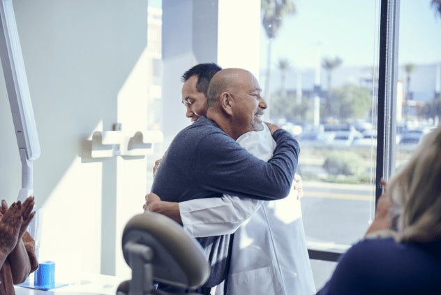 A Doctor hugging his happy patient in an exam room. 