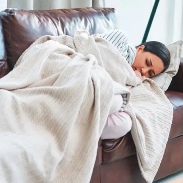 A woman is sleeping on a couch under a blanket