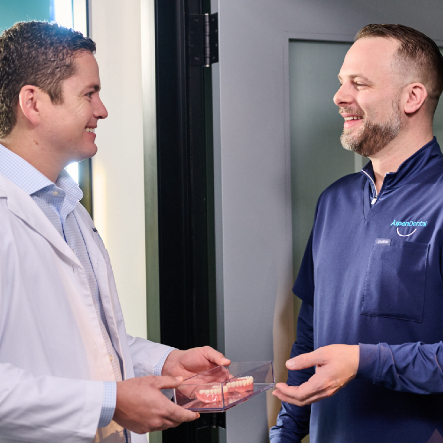 Aspen Dental doctors speak as they pass a pair of dentures to each other. 