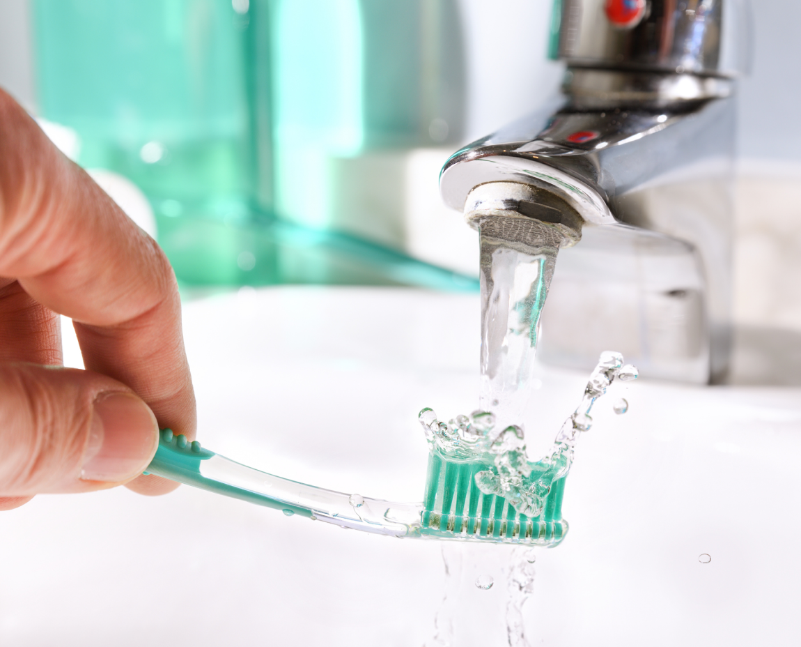 Rinsing a toothbrush under a running tap, water splashing on bristles.
