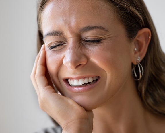 Woman holding her cheek in discomfort, indicating pain in the mouth possibly due to dental issues like impacted wisdom teeth.