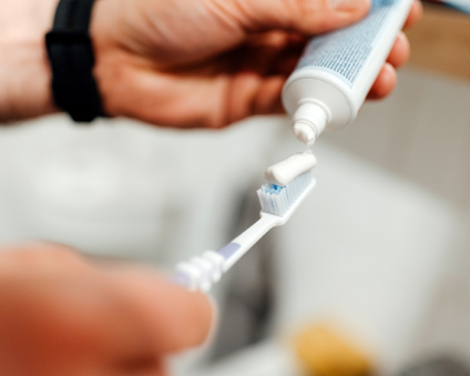 A hand squeezes toothpaste onto a toothbrush. 