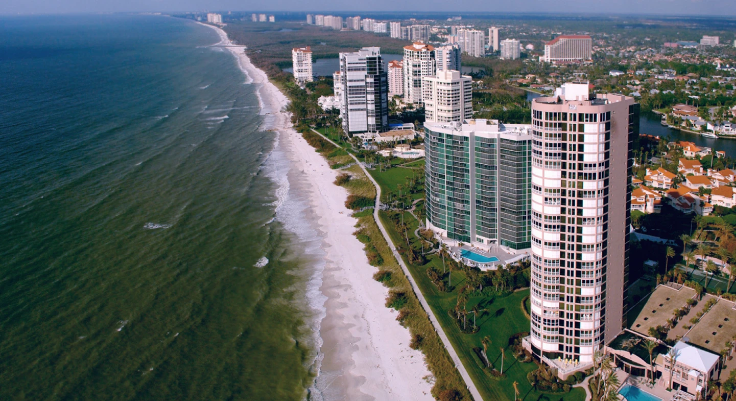 An aerial view of buildings along the shoreline in Naples, FL at midday